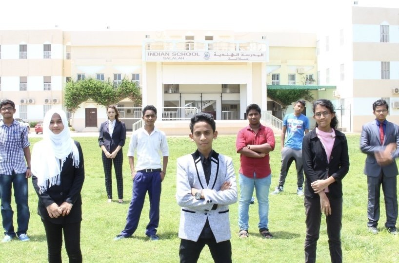 Ajmal Basheer and the student live-streaming team standing on the lawn in front of Indian School Salalah
