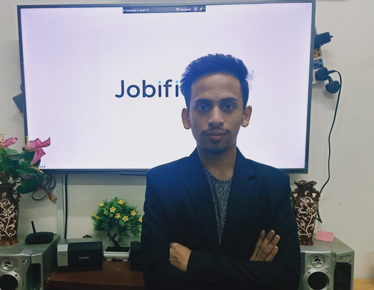 Ajmal Basheer in a dark blazer, arms crossed, in front of a TV screen showing the Jobified logo