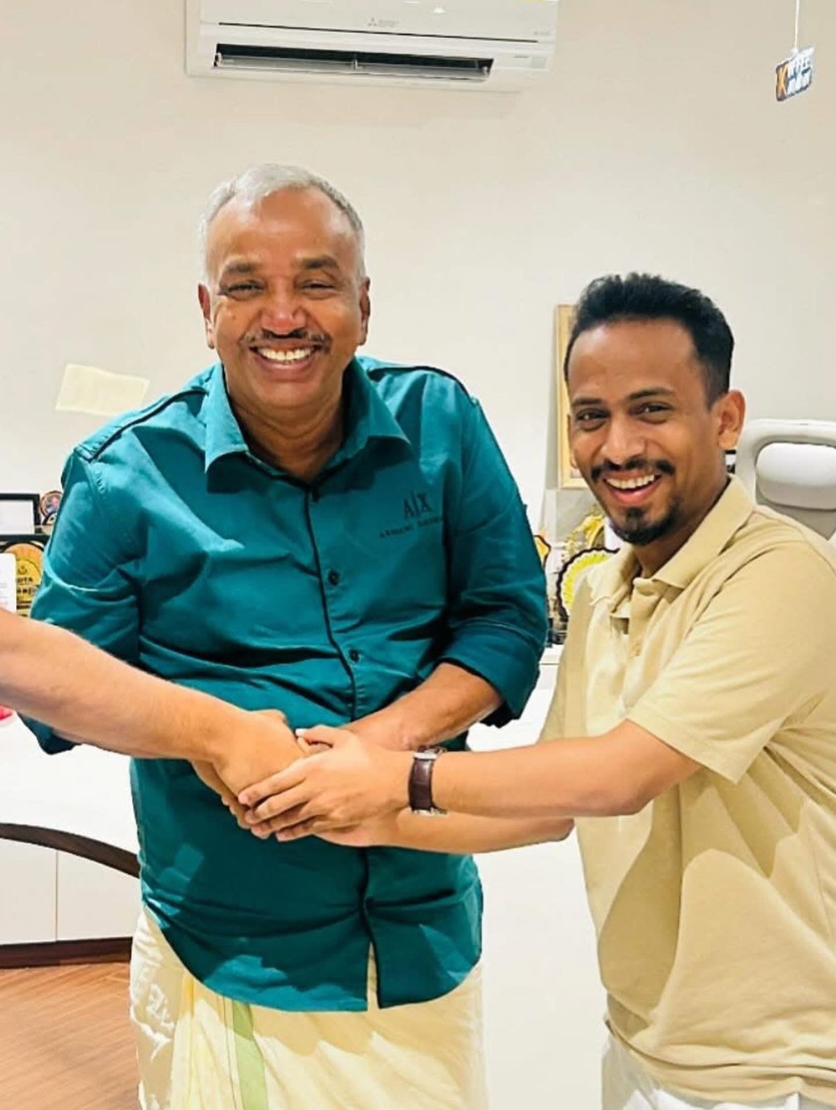 Ajmal Basheer and mentor Karadan Sulaiman laughing together, hands joined, in an office