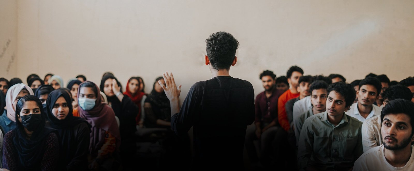 Ajmal Basheer addressing a full room of students, back to camera, hand raised